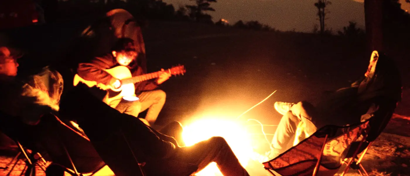 Friends in camp chairs round a big campfire as the light goes