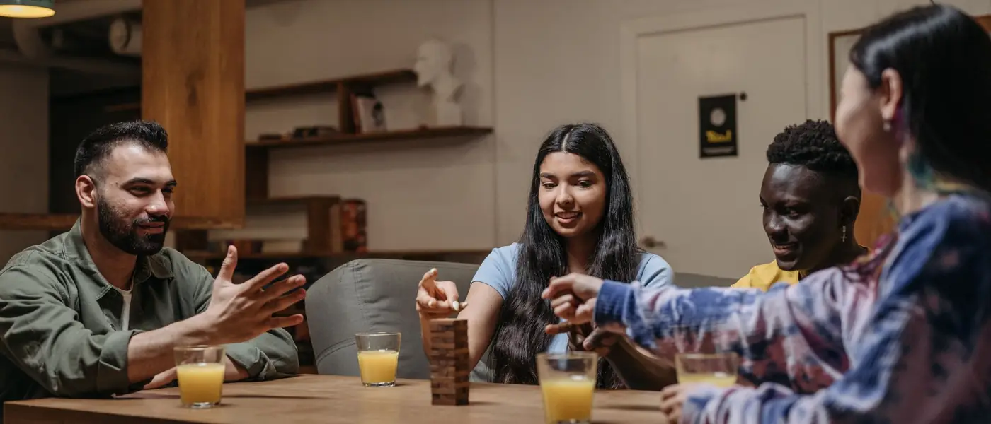 Six friends piled onto a living-room sofa, arms in the air, mid-laugh