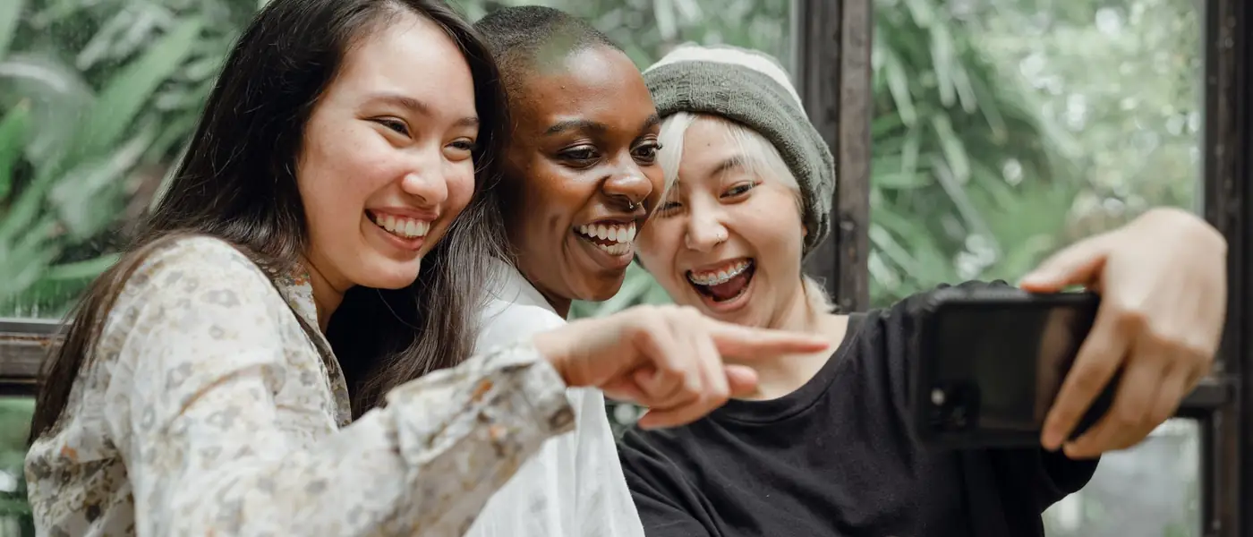 Three friends crowded round a single phone, laughing at what's on it