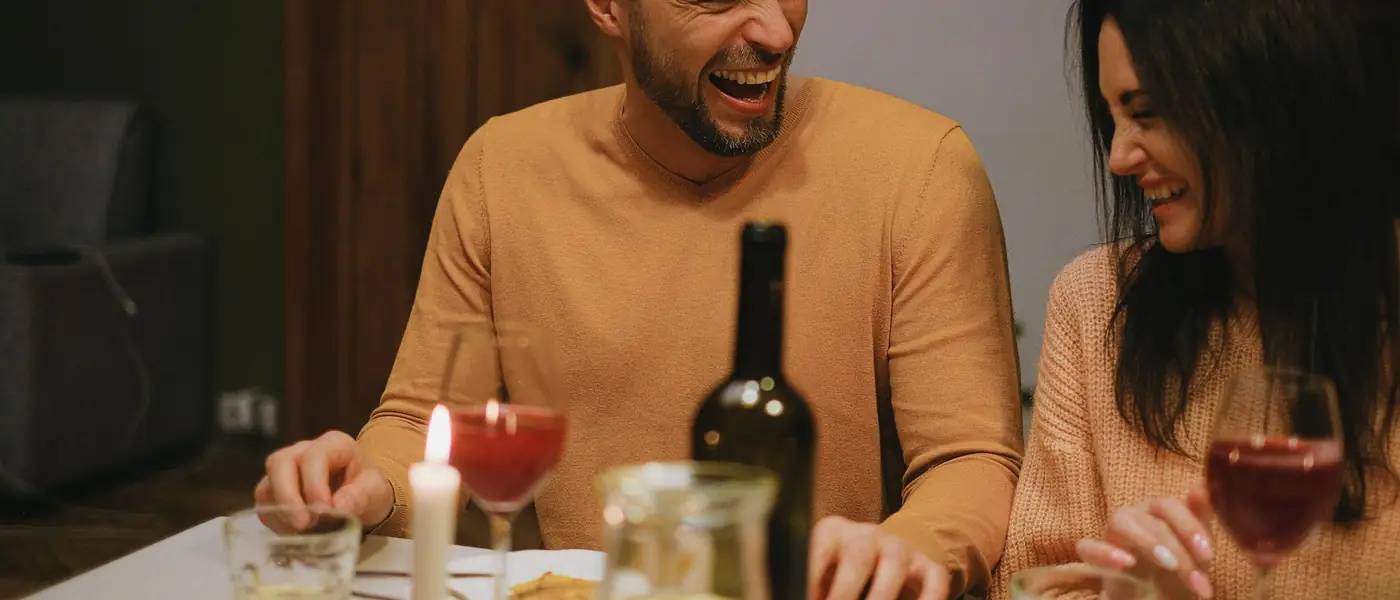 Two people laughing across a candlelit table at home